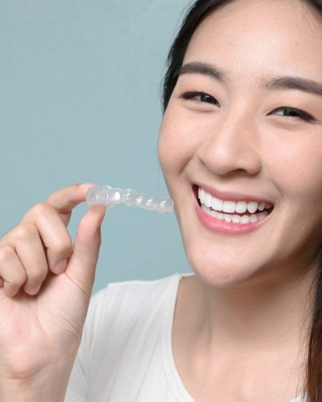 Smiling woman holding Invisalign clear aligner