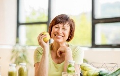Smiling woman sitting at table and holding an apple