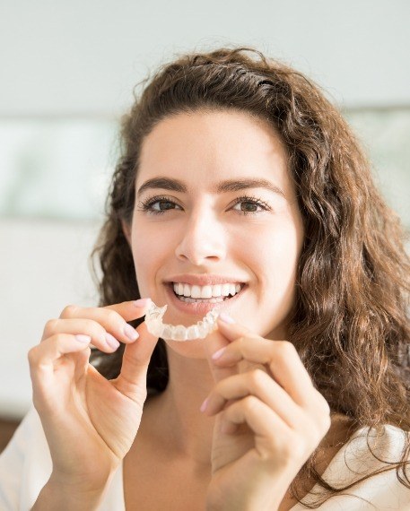 Woman with curly hair holding Invisalign tray