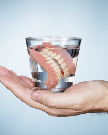 Hand holding a glass of water soaking dentures