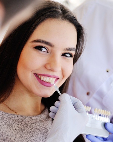 Woman in dental chair smiling while dentist holds shade guide to her teeth