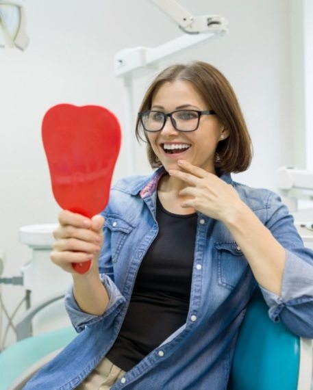 Woman in dental chair admiring her smile in mirror