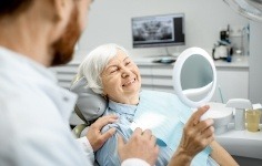 Senior dental patient admiring her smile in mirror