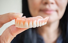 Dentist holding upper arch of dentures with thumb and forefinger