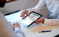  Two people at desk zooming in on “Dental Insurance” on digital tablet