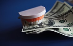 Set of artificial teeth biting down on $100 bills with dark blue background
