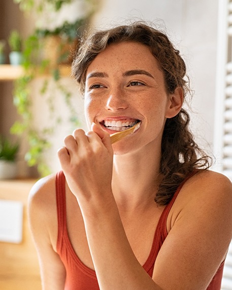 A young woman brushing her teeth in front of a bathroom mirror