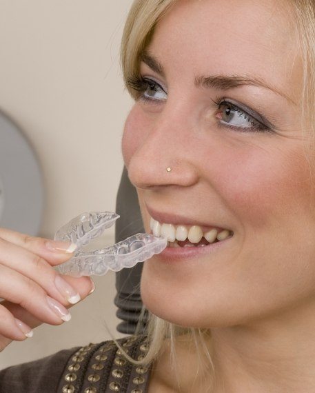 Smiling blonde woman holding Invisalign aligner