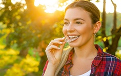 Woman inserting an Invisalign tray with trees in the background