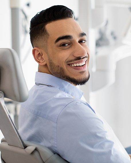 Bearded man in dental chair looking over shoulder and smiling