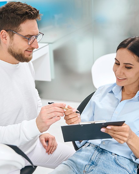 Woman in dental chair signing forms on clipboard