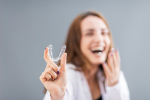 Woman laughing and holding Invisalign aligner