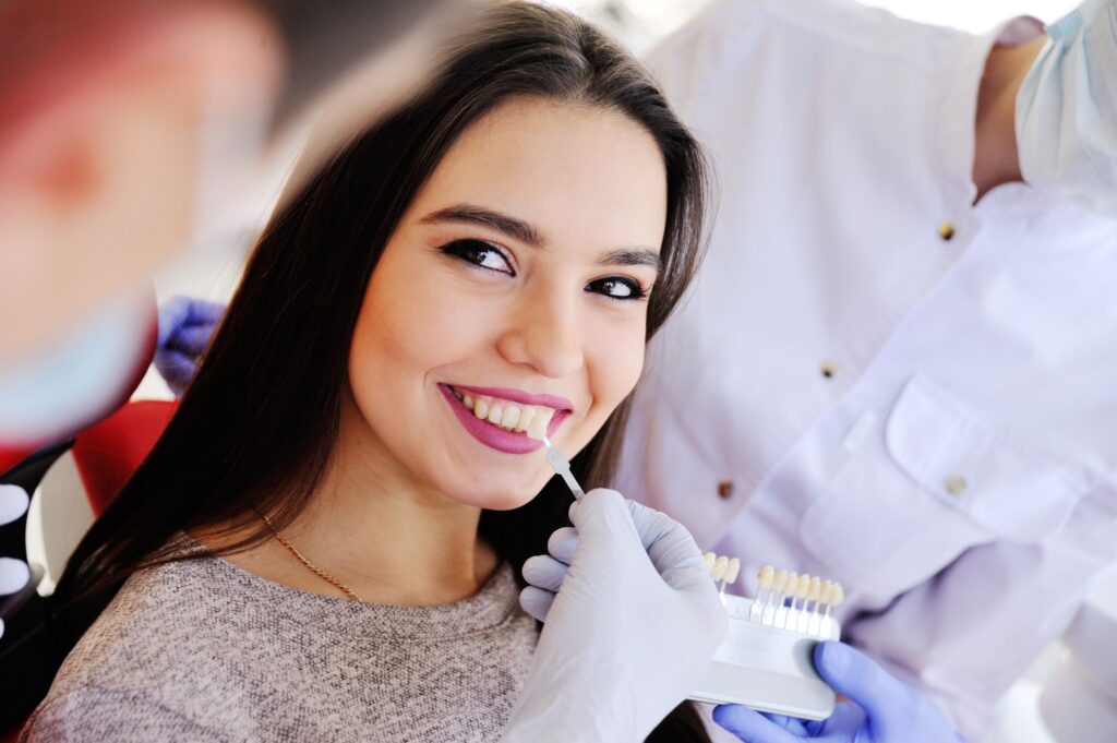 Dentist holding shade guide to woman's teeth