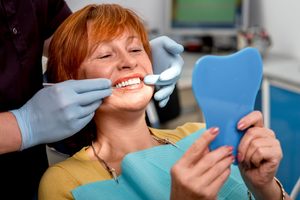 Woman looking at teeth in mirror with dentist touching corners of her mouth